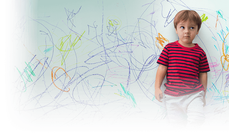 Young boy standing in front of a wall covered in colorful crayon drawings