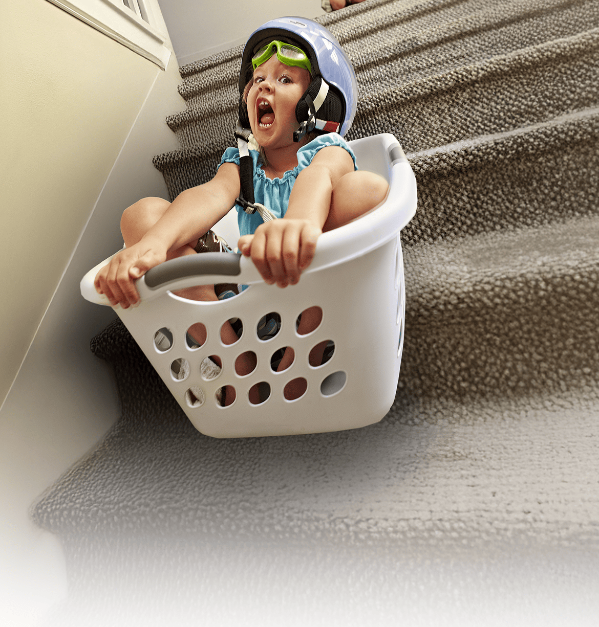 Playful child wearing goggles and helmet in a laundry basket, representing home care ease with ZELSUVMI